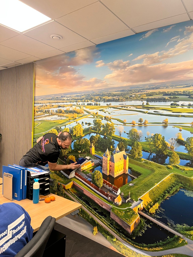 Cornelissen monteert een grote wandvisual met een kasteel en rivierlandschap in een kantoor
